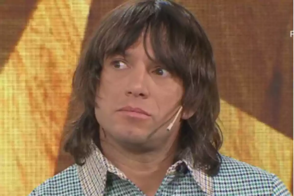 Hombre de cabello largo y oscuro con camisa a cuadros y micrófono de diadema en un set de televisión Hombre de cabello largo y oscuro con camisa a cuadros y micrófono de diadema en un set de televisión