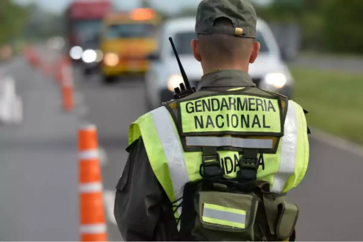 National Gendarmerie officer seen from behind conducting a vehicle check on a road with orange cones and vehicles in the background National Gendarmerie officer seen from behind conducting a vehicle check on a road with orange cones and vehicles in the background