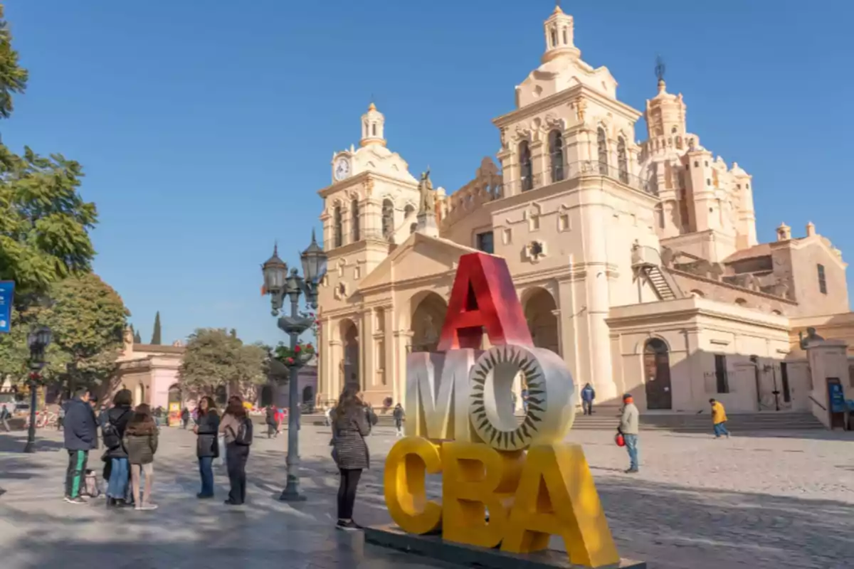 Personas caminando frente a la Catedral de Córdoba con un colorido cartel de letras grandes que dice Amo CBA en primer plano