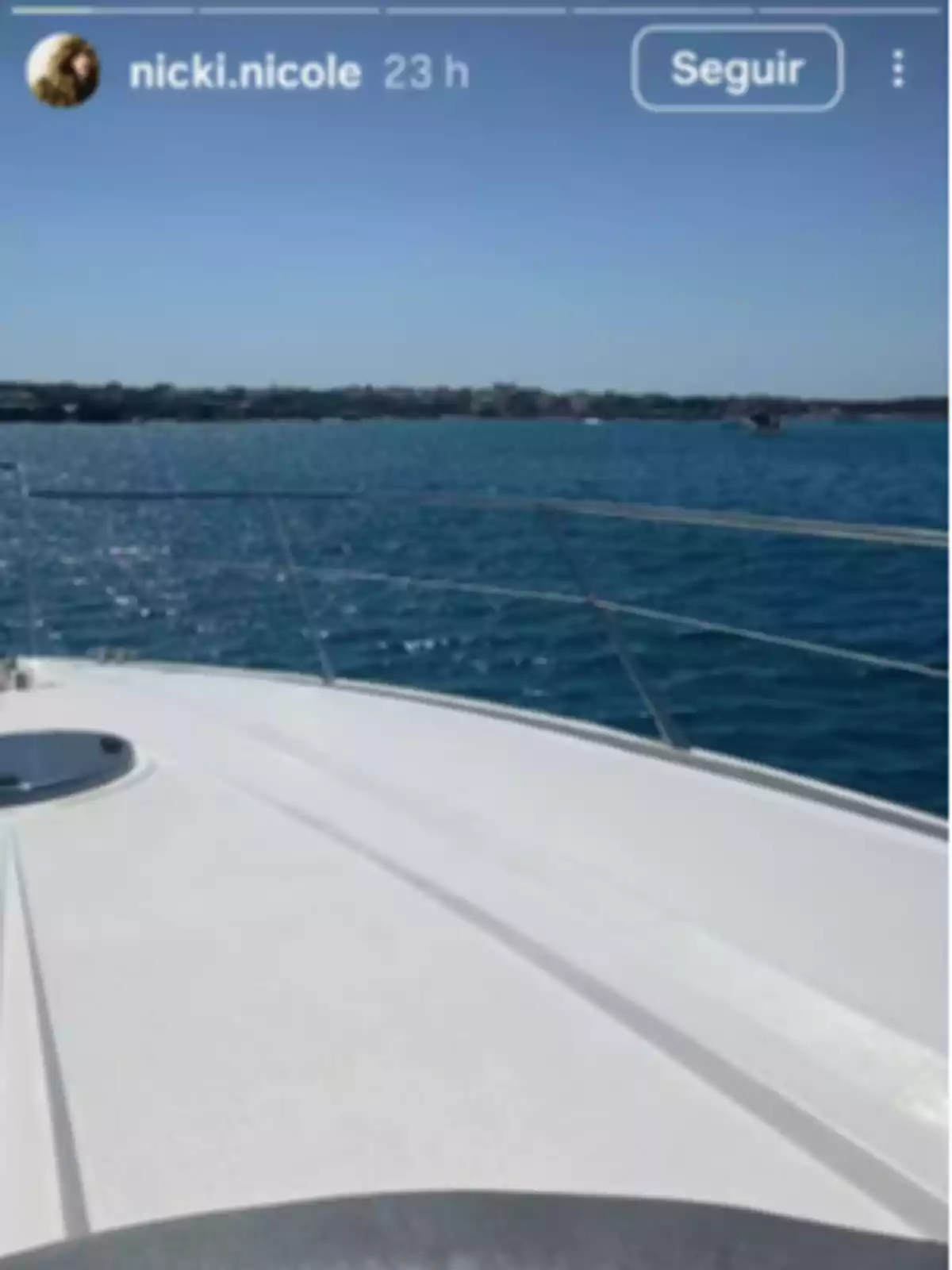 View from the bow of a yacht sailing in blue waters with the coast in the background under a clear sky View from the bow of a yacht sailing in blue waters with the coast in the background under a clear sky