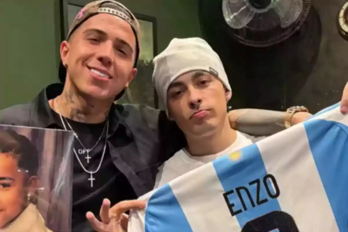Two young men pose together, one holding a photo of a child and the other showing an Argentina national team jersey with the name Enzo. Two young men pose together, one holding a photo of a child and the other showing an Argentina national team jersey with the name Enzo.