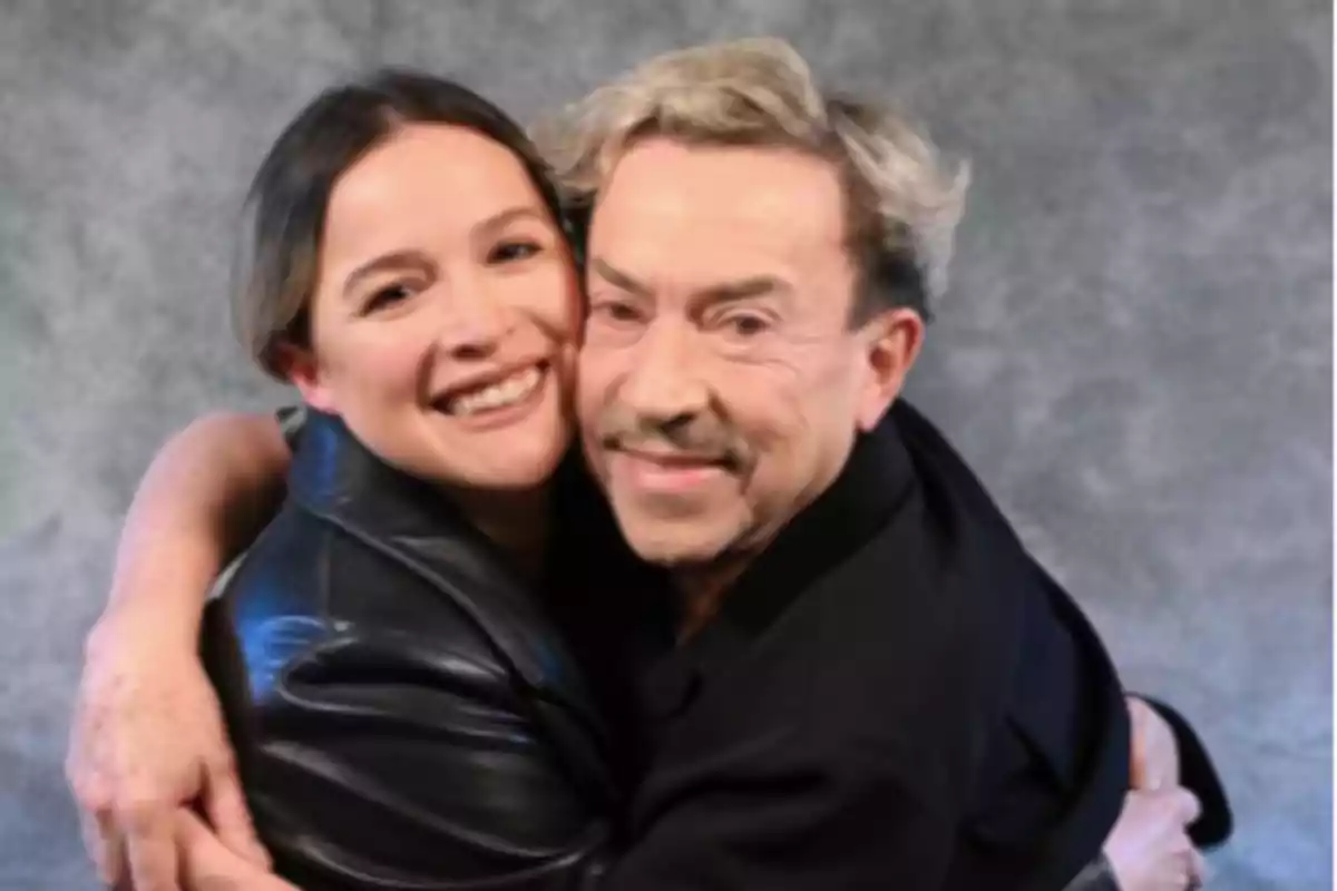 Two smiling people hug in front of a gray background