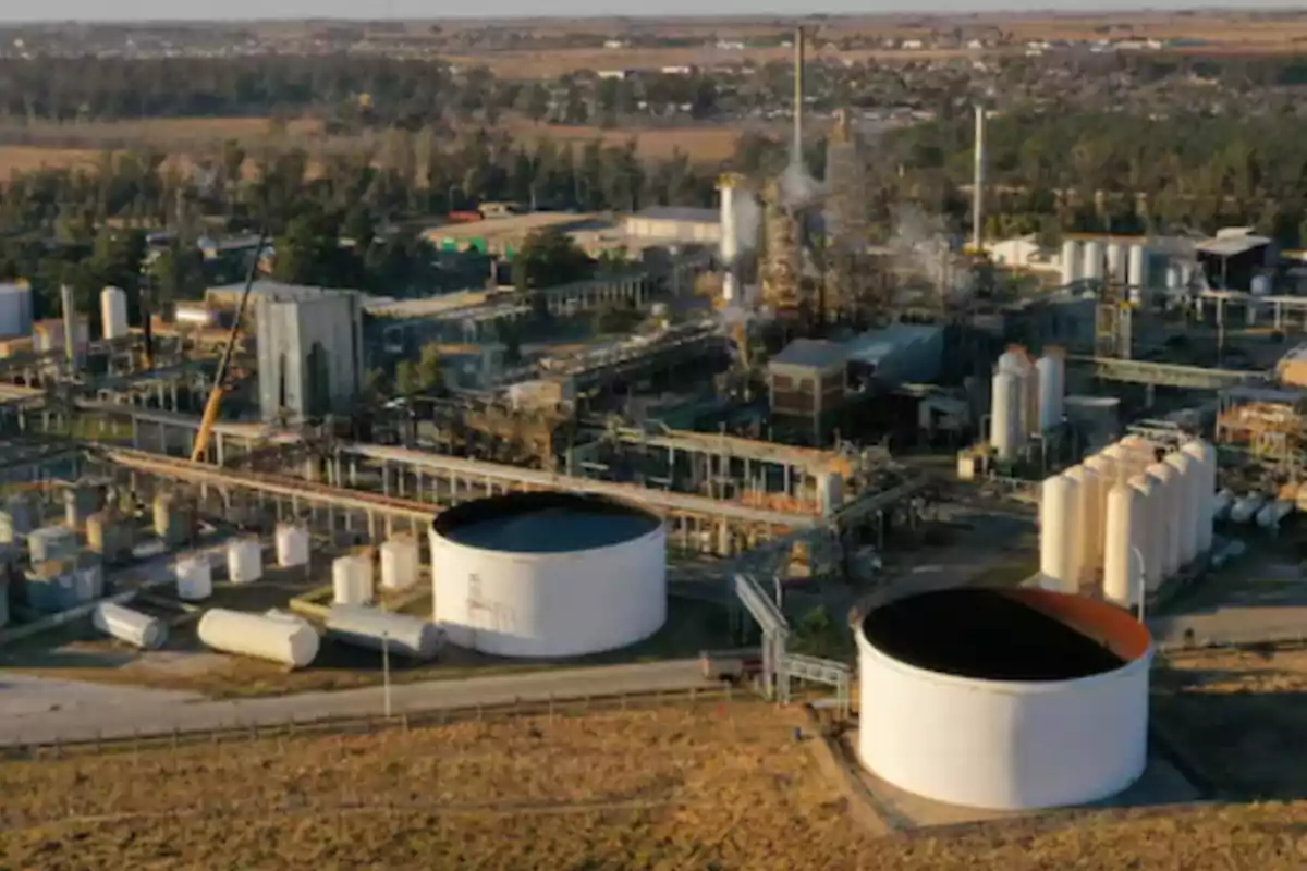 Aerial view of an industrial plant with storage tanks and metal structures surrounded by vegetation and roads