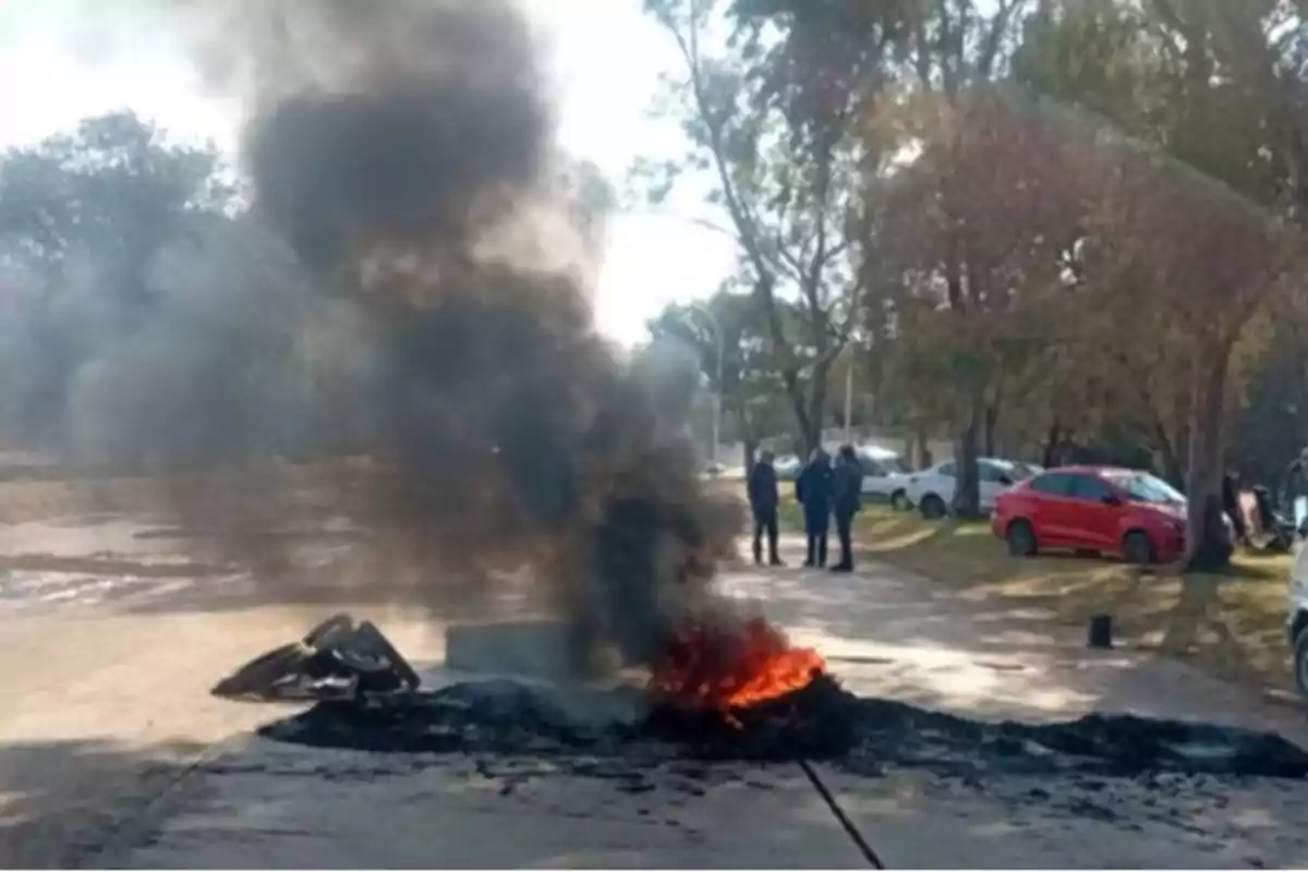 Burning tires on a street with black smoke and people watching from a distance Burning tires on a street with black smoke and people watching from a distance