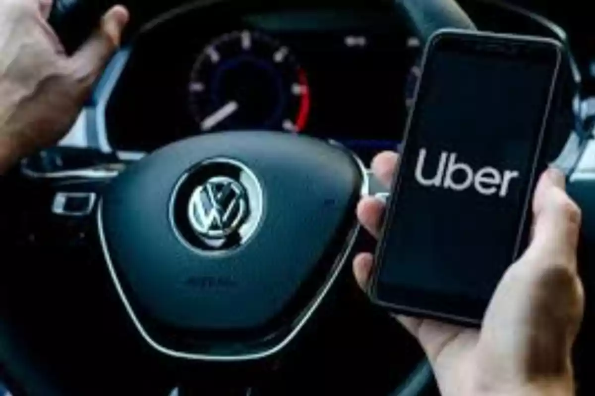 Person holding a phone with the Uber app open while driving a Volkswagen car Person holding a phone with the Uber app open while driving a Volkswagen car