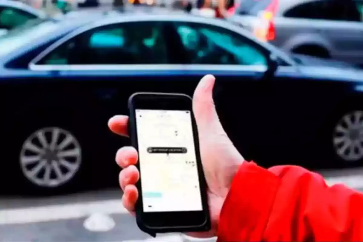 Person wearing a red jacket holds a mobile phone with a ride-hailing app open in front of a black car on the street Person wearing a red jacket holds a mobile phone with a ride-hailing app open in front of a black car on the street