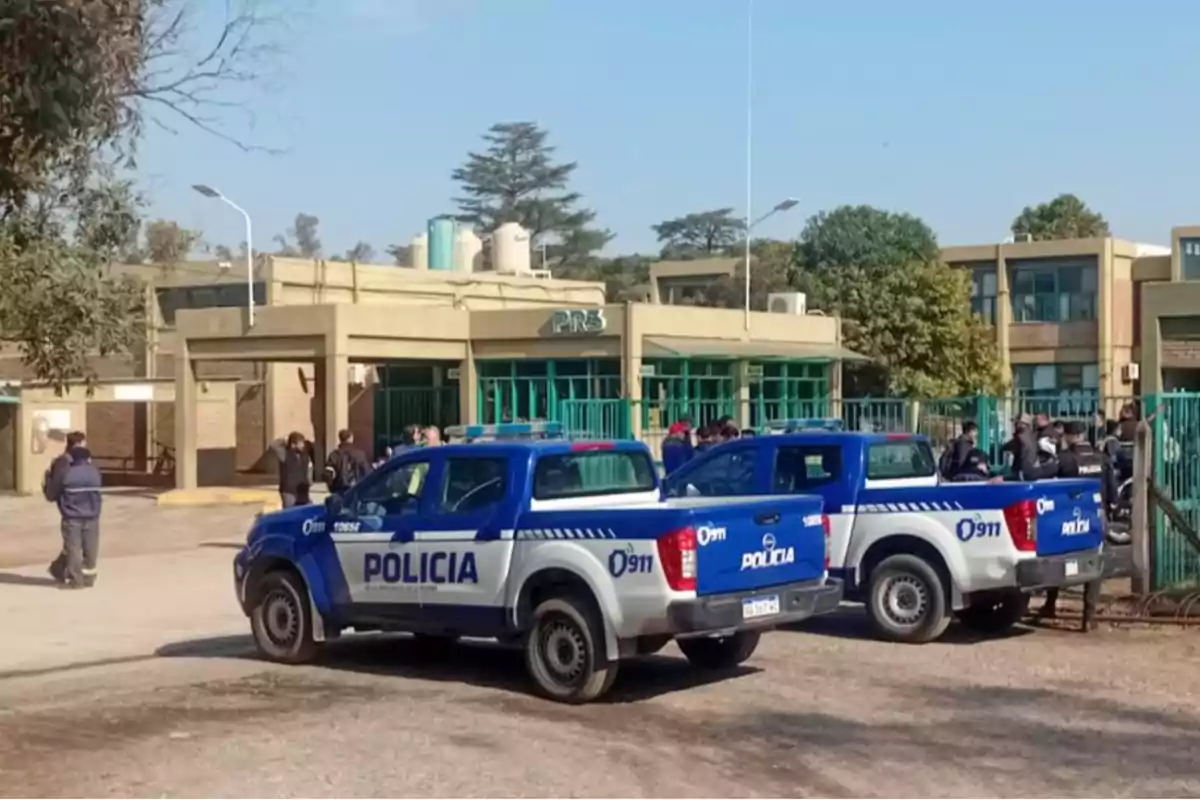 Dos camionetas de la policía estacionadas frente a un edificio con varias personas reunidas en la entrada Dos camionetas de la policía estacionadas frente a un edificio con varias personas reunidas en la entrada