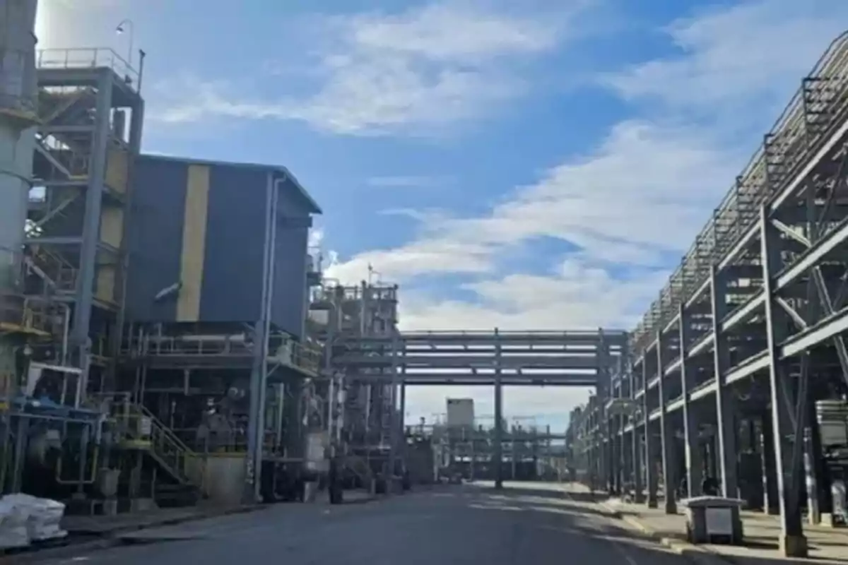 Vista de una planta industrial con estructuras metálicas y tuberías bajo un cielo parcialmente nublado