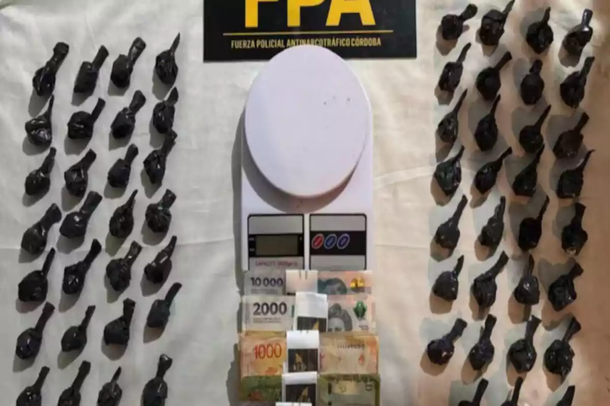 Black bags arranged in rows next to a digital scale and several bills on a white table with a Córdoba Anti-Narcotics Police Force sign in the background.