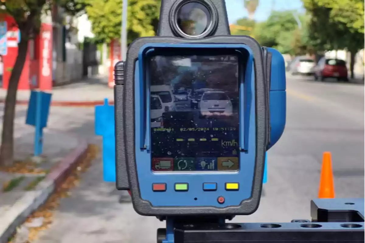 Speed radar device pointing toward a street with several cars and an orange cone in the background Speed radar device pointing toward a street with several cars and an orange cone in the background