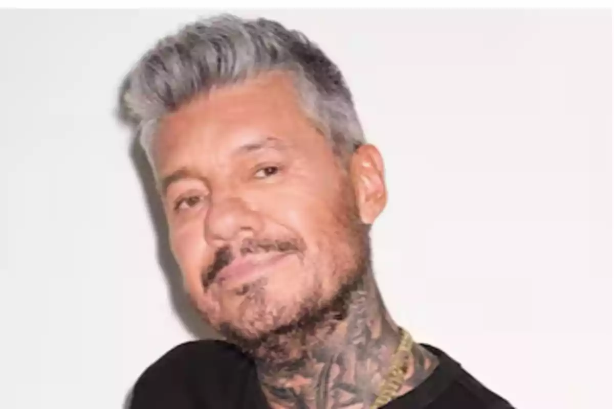 Gray-haired man with a beard, tattoos on his neck, and a black t-jersey looking at the camera