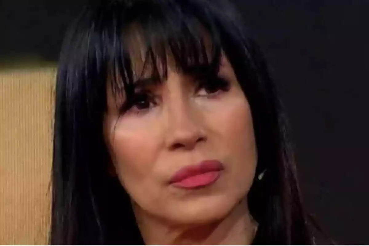 Dark-haired woman with bangs, serious expression, and pink lips in an indoor setting