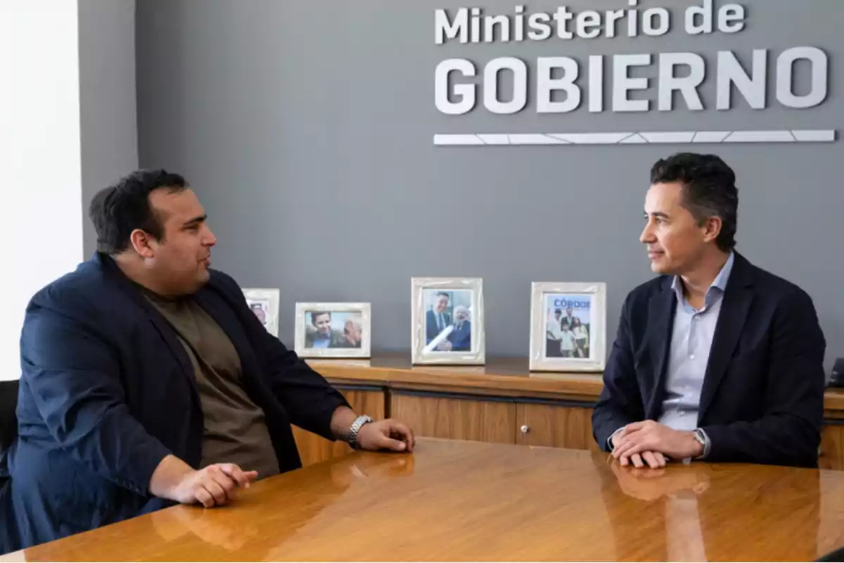 Two men are talking while sitting at a wooden table in an office with a Two men are talking while sitting at a wooden table in an office with a