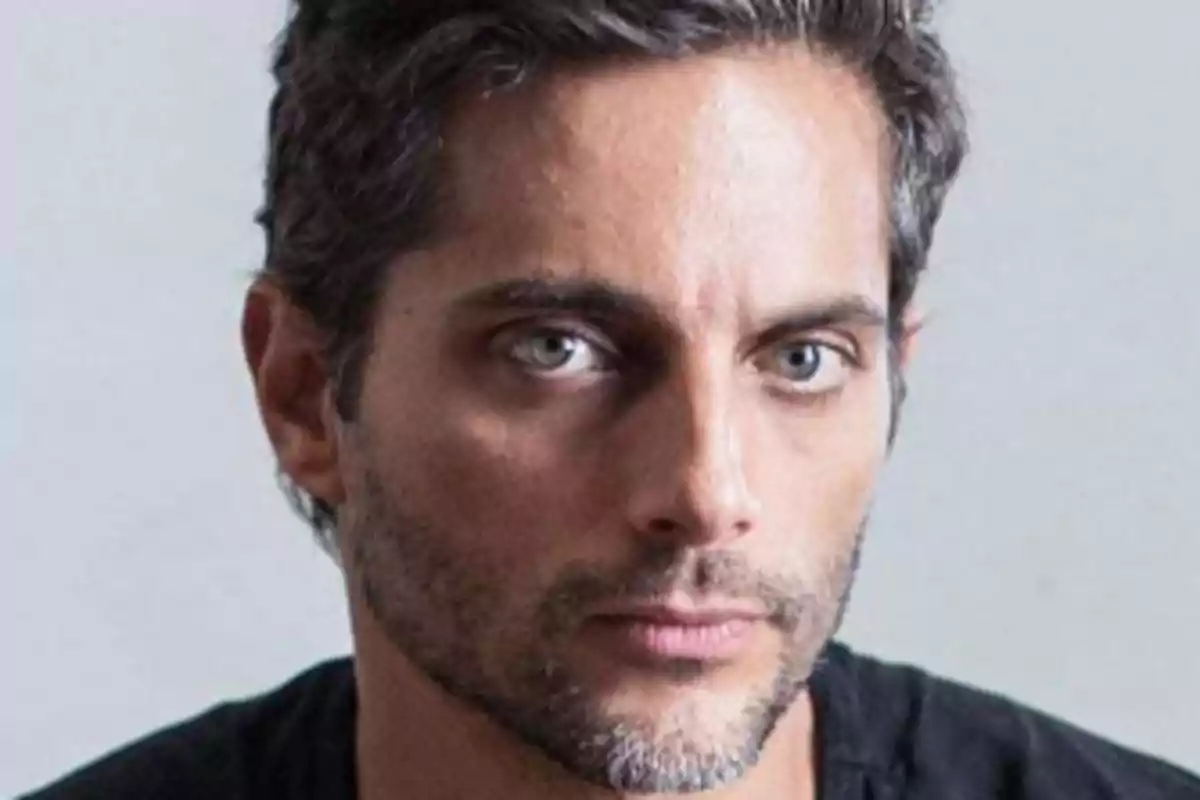 Man with short hair and a light beard looking forward with a serious expression.
