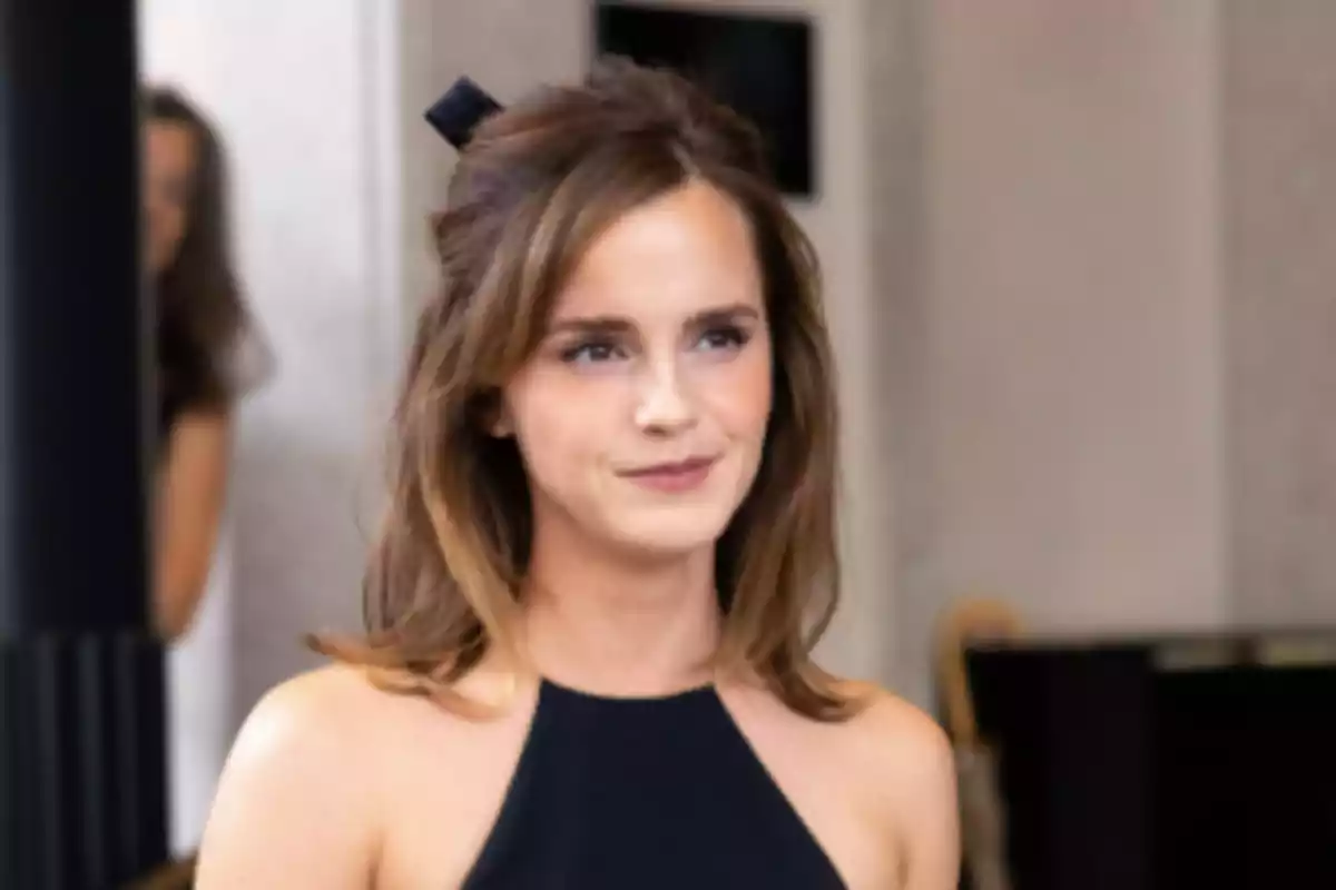 Mujer joven de cabello castaño y suelto con un vestido negro sin mangas en un ambiente interior elegante