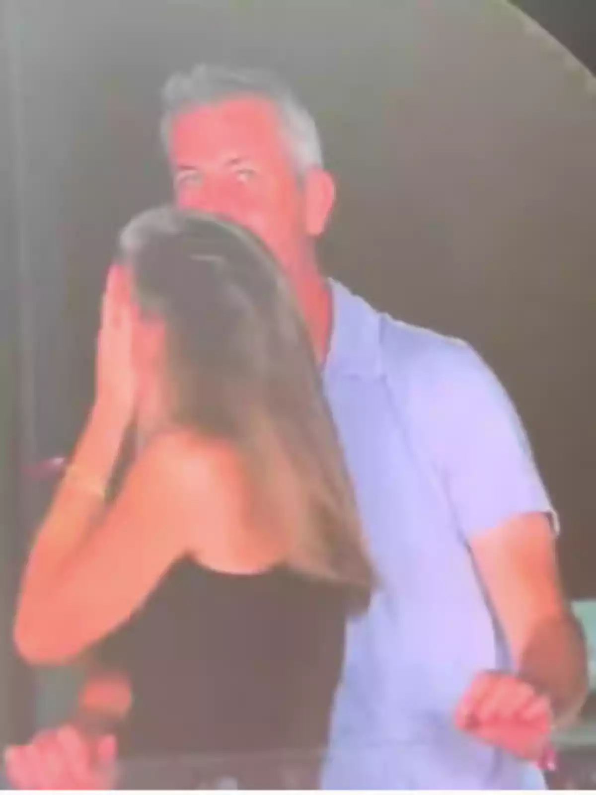 Una mujer cubre su rostro con la mano mientras un hombre de cabello canoso la observa en un ambiente nocturno Una mujer cubre su rostro con la mano mientras un hombre de cabello canoso la observa en un ambiente nocturno