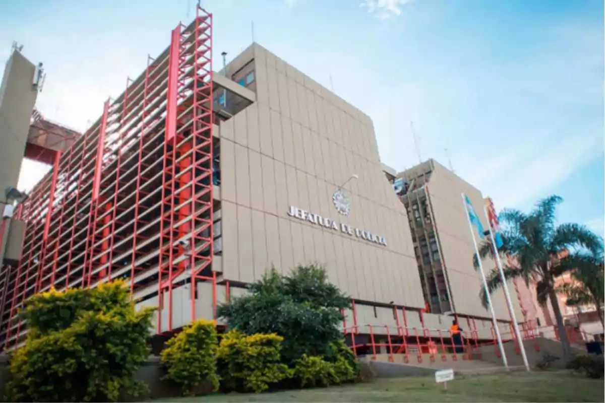 Edificio grande de la Jefatura de Policía con estructura moderna, jardines al frente y banderas izadas