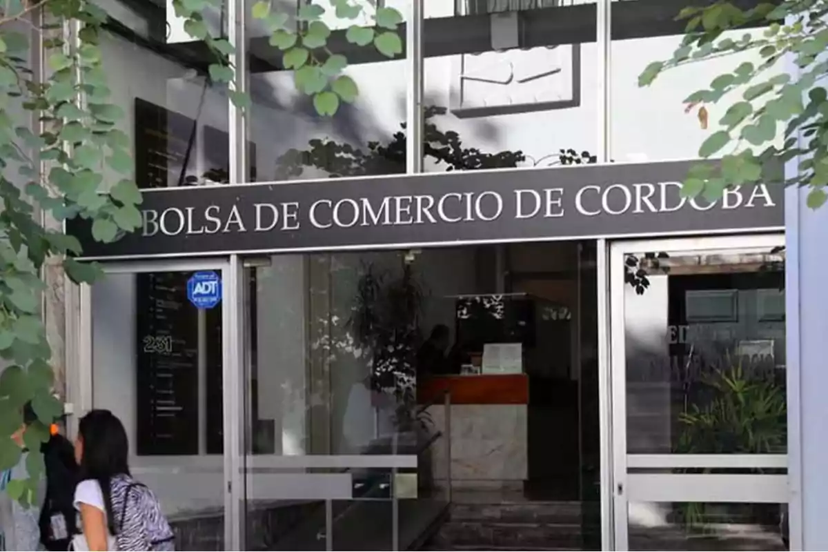Entrada principal de la Bolsa de Comercio de Córdoba con personas ingresando y plantas alrededor