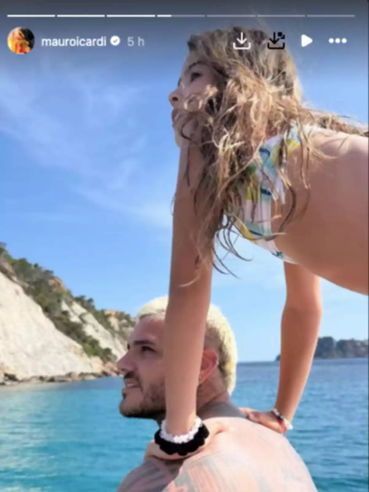 Hombre con el cabello corto y rubio en el mar lleva a una niña sobre sus hombros mientras disfrutan de un día soleado junto a un acantilado Hombre con el cabello corto y rubio en el mar lleva a una niña sobre sus hombros mientras disfrutan de un día soleado junto a un acantilado