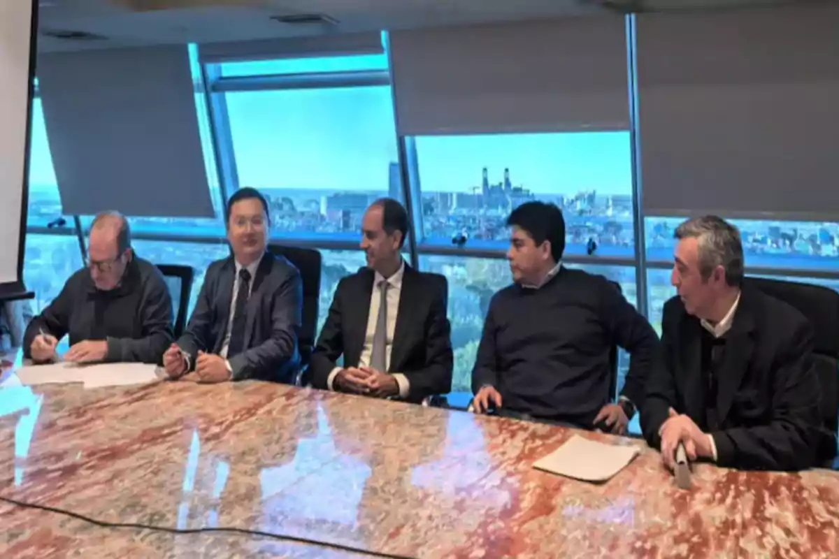 Cinco hombres sentados en una sala de juntas con una mesa de mármol y una gran ventana al fondo que muestra una ciudad