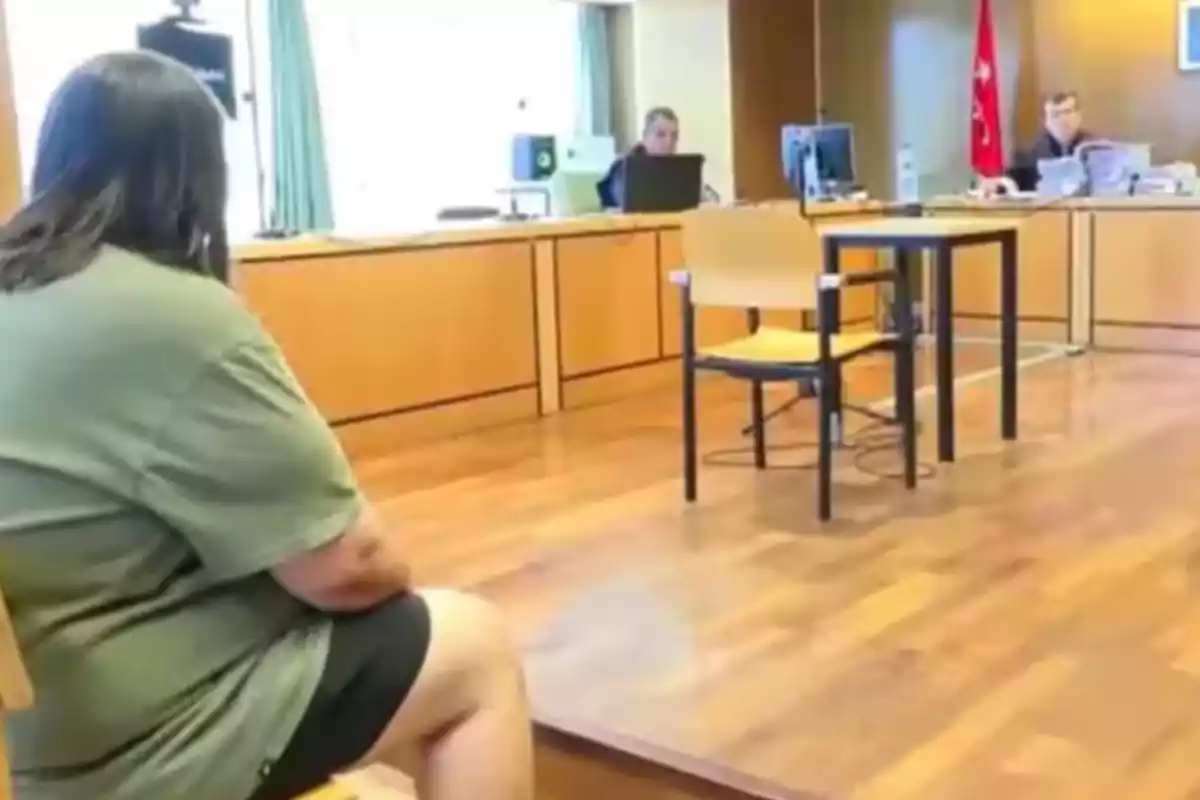 A person sitting in a courtroom in front of two officials and desks
