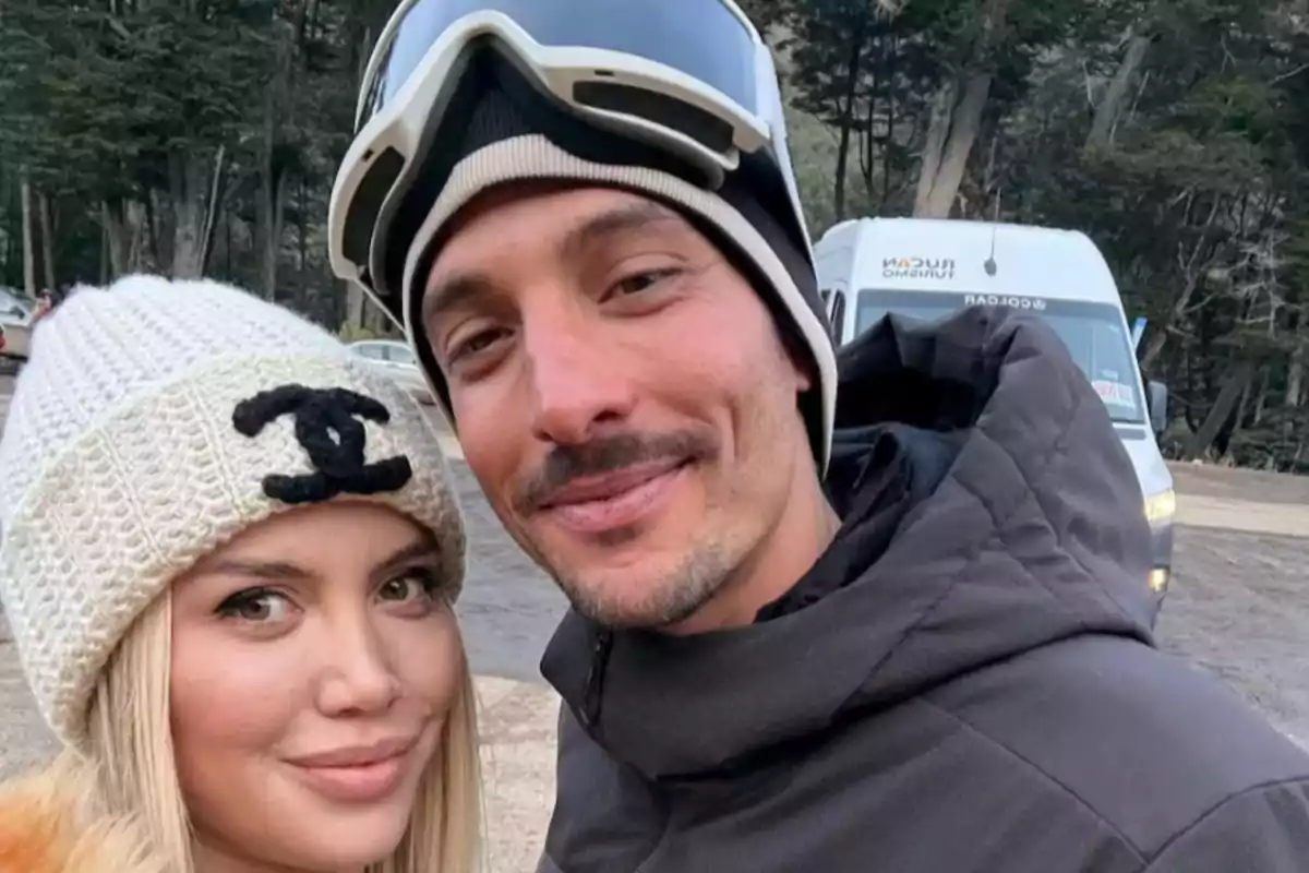Pareja sonriente con ropa de invierno posando al aire libre frente a un bosque y una camioneta blanca Pareja sonriente con ropa de invierno posando al aire libre frente a un bosque y una camioneta blanca