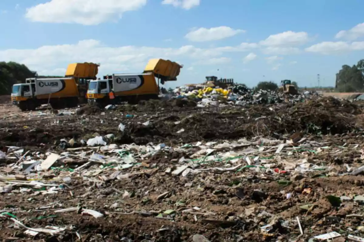 Camiones de basura descargando desechos en un vertedero al aire libre bajo un cielo parcialmente nublado Camiones de basura descargando desechos en un vertedero al aire libre bajo un cielo parcialmente nublado