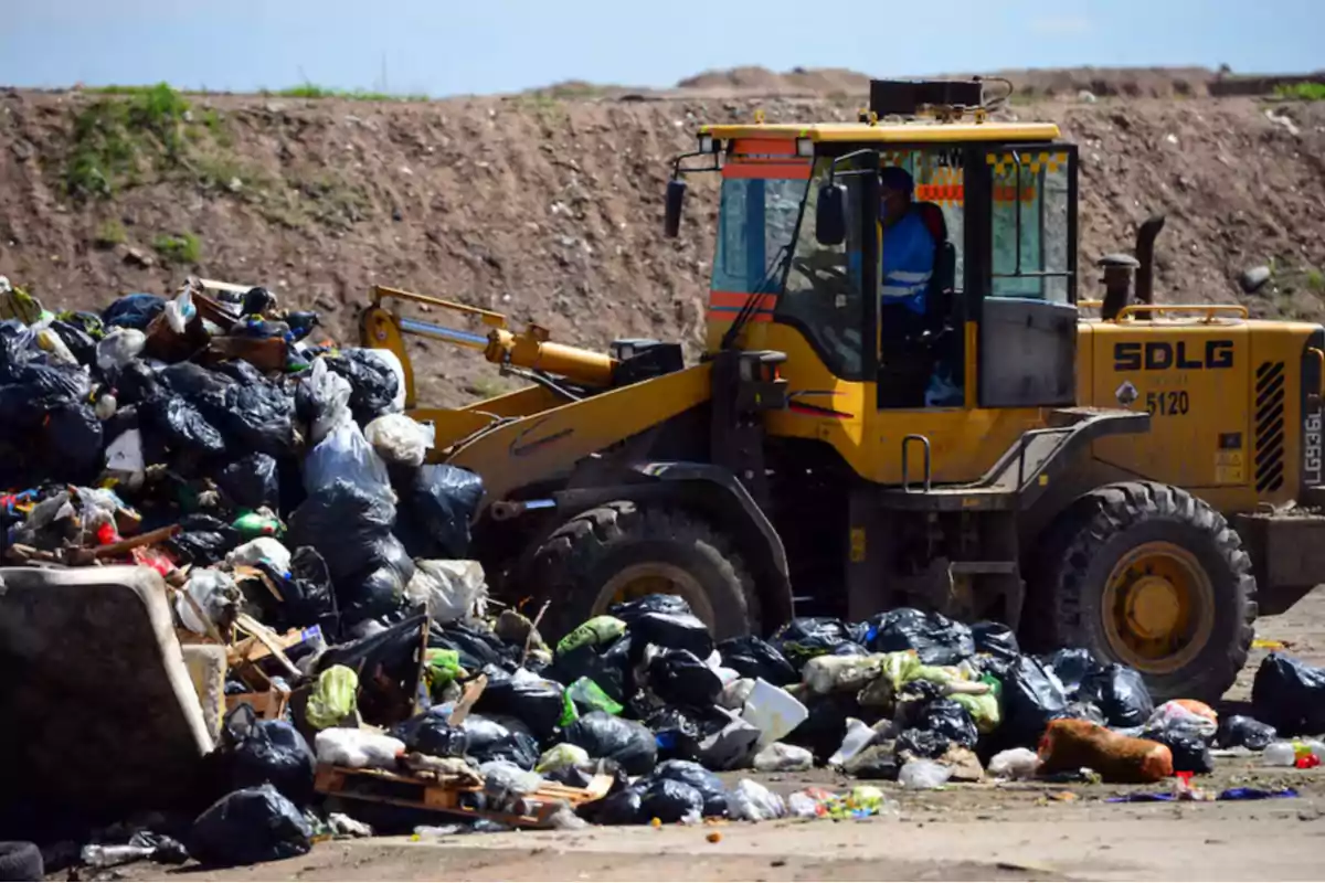 Una retroexcavadora mueve una gran cantidad de bolsas de basura en un vertedero al aire libre