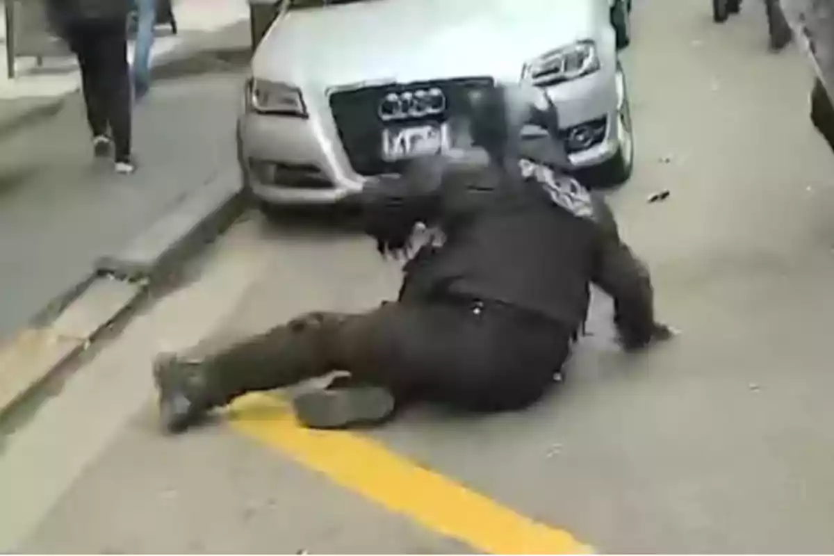 Un policía cae al suelo frente a un automóvil plateado en una calle urbana