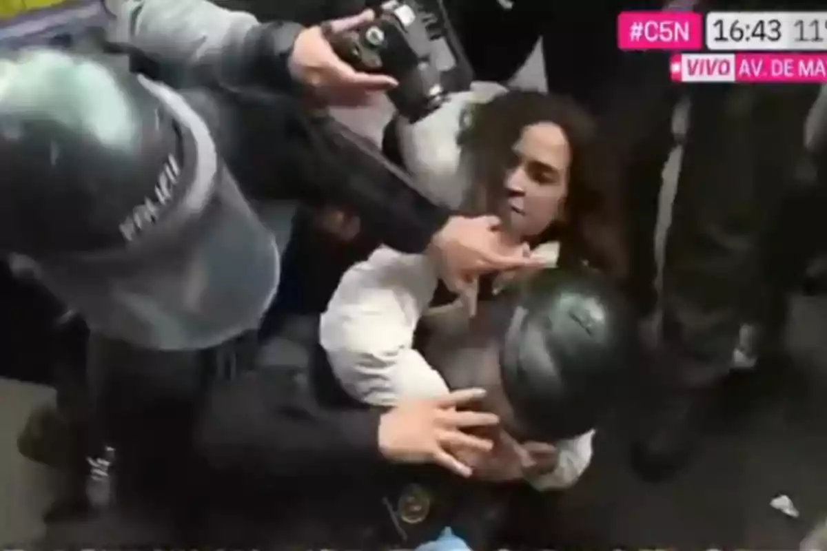 A person is held on the ground by several police officers while a photographer captures the moment at a protest.