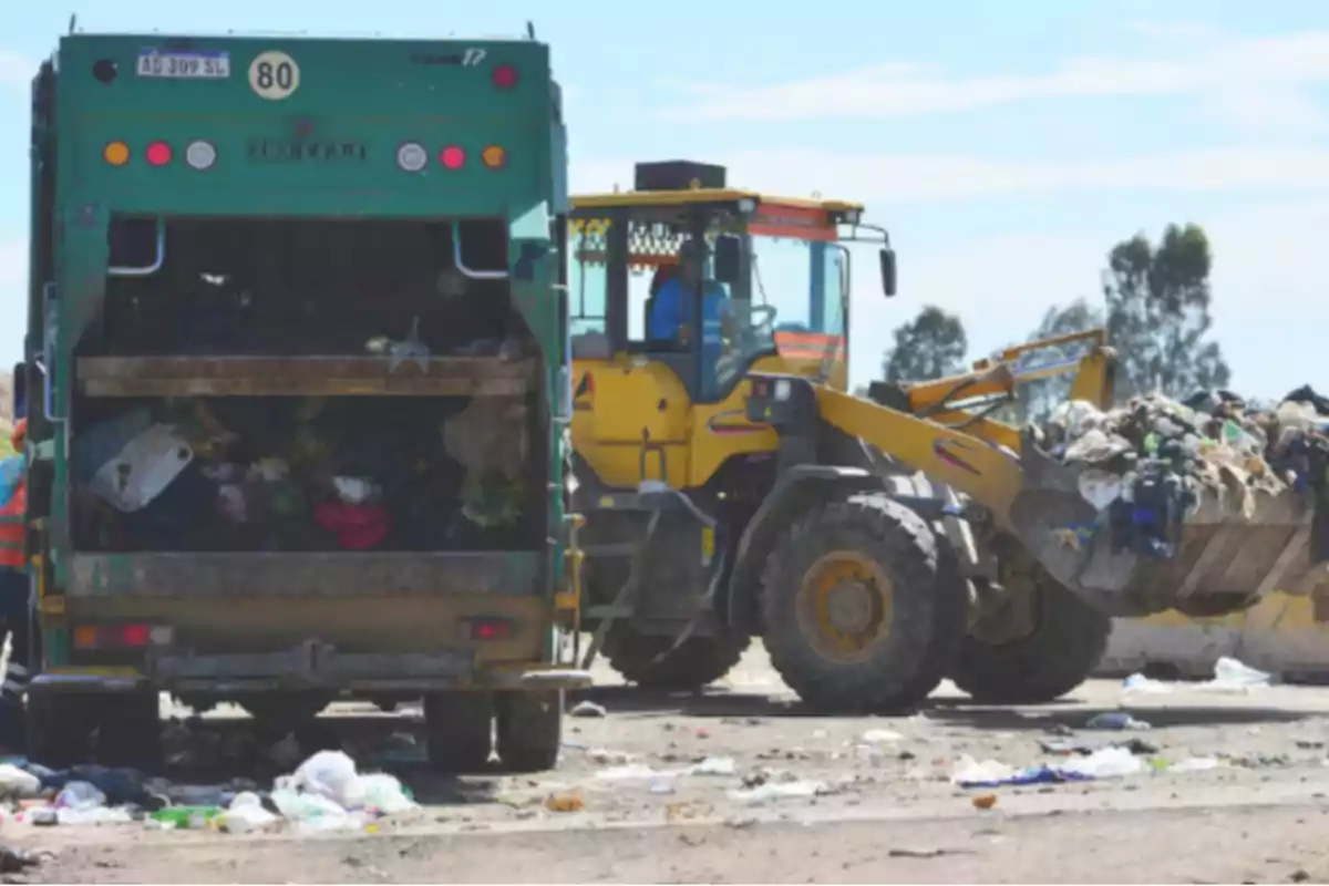Un camión de basura y una retroexcavadora trabajan juntos en un vertedero moviendo residuos sólidos Un camión de basura y una retroexcavadora trabajan juntos en un vertedero moviendo residuos sólidos