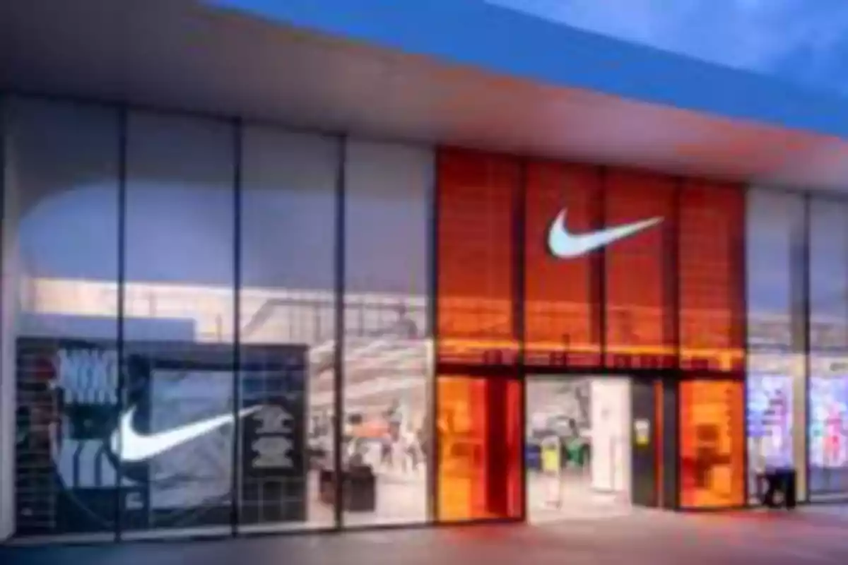 Fachada de una tienda Nike con paredes de vidrio y paneles naranjas iluminados