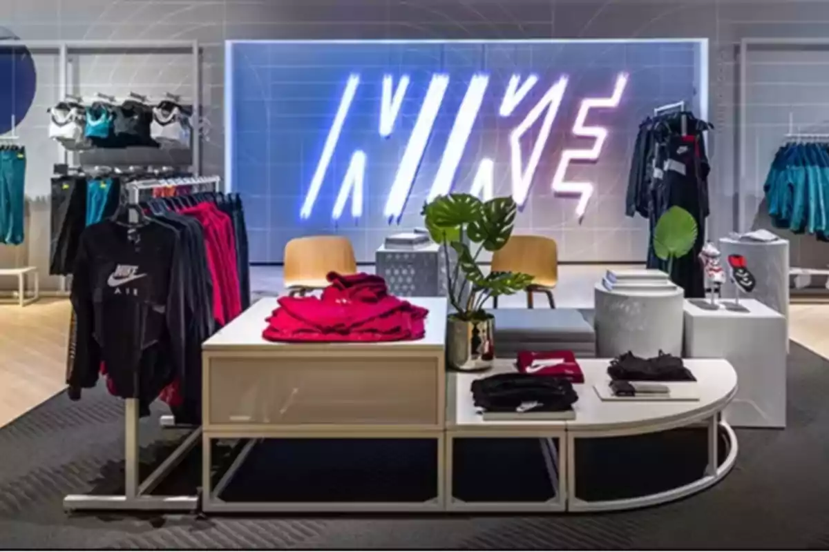 Tienda de ropa deportiva Nike con prendas exhibidas y un letrero luminoso de la marca al fondo Tienda de ropa deportiva Nike con prendas exhibidas y un letrero luminoso de la marca al fondo