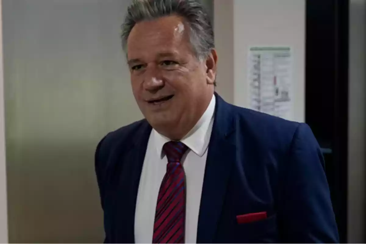 Hombre de cabello canoso con traje azul y corbata roja sonriendo en un entorno de oficina