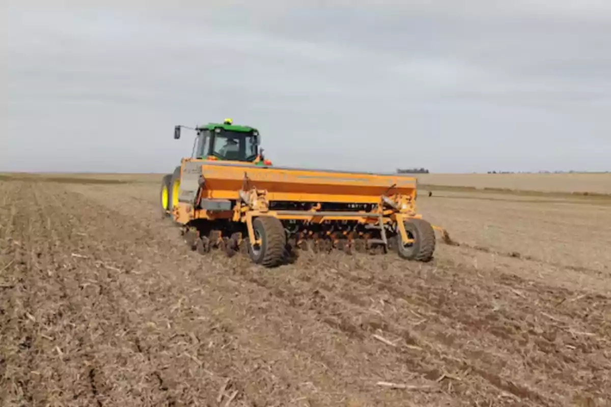 Tractor agrícola trabajando en un campo seco con una sembradora amarilla Tractor agrícola trabajando en un campo seco con una sembradora amarilla