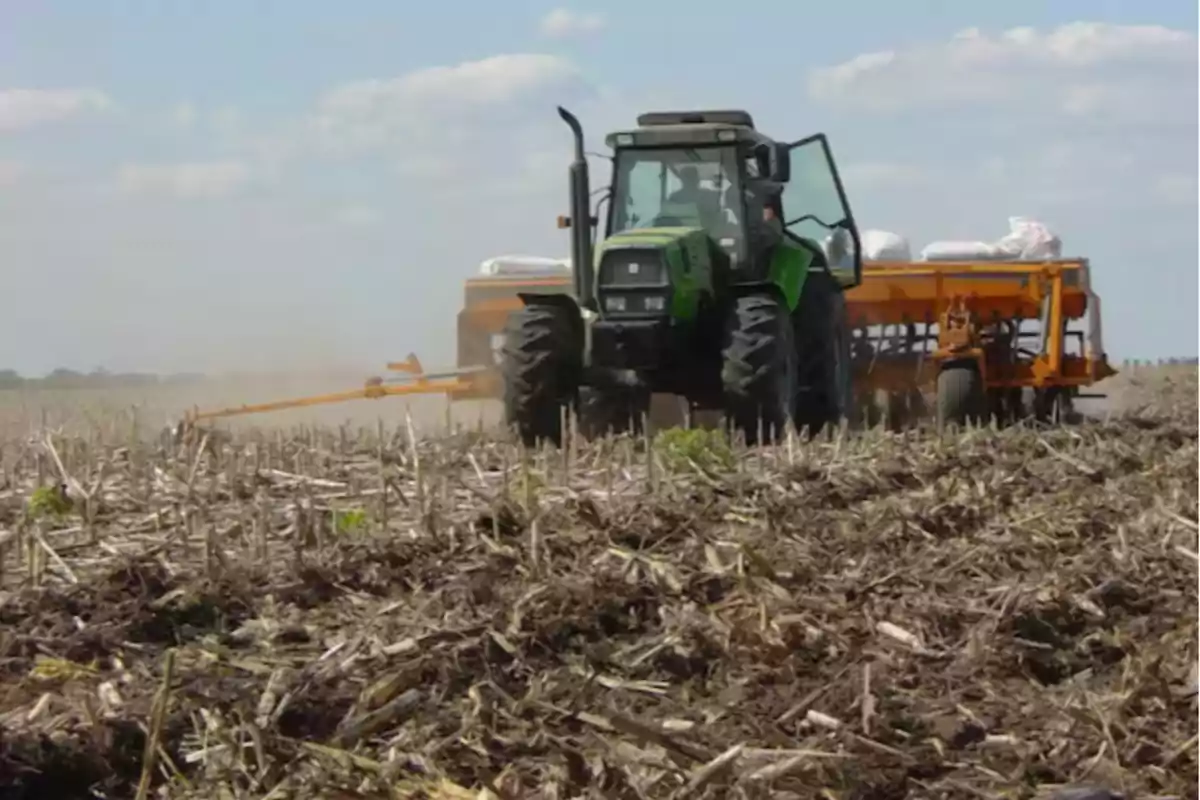 Tractor verde trabajando en un campo seco con restos de cosecha y cielo parcialmente nublado