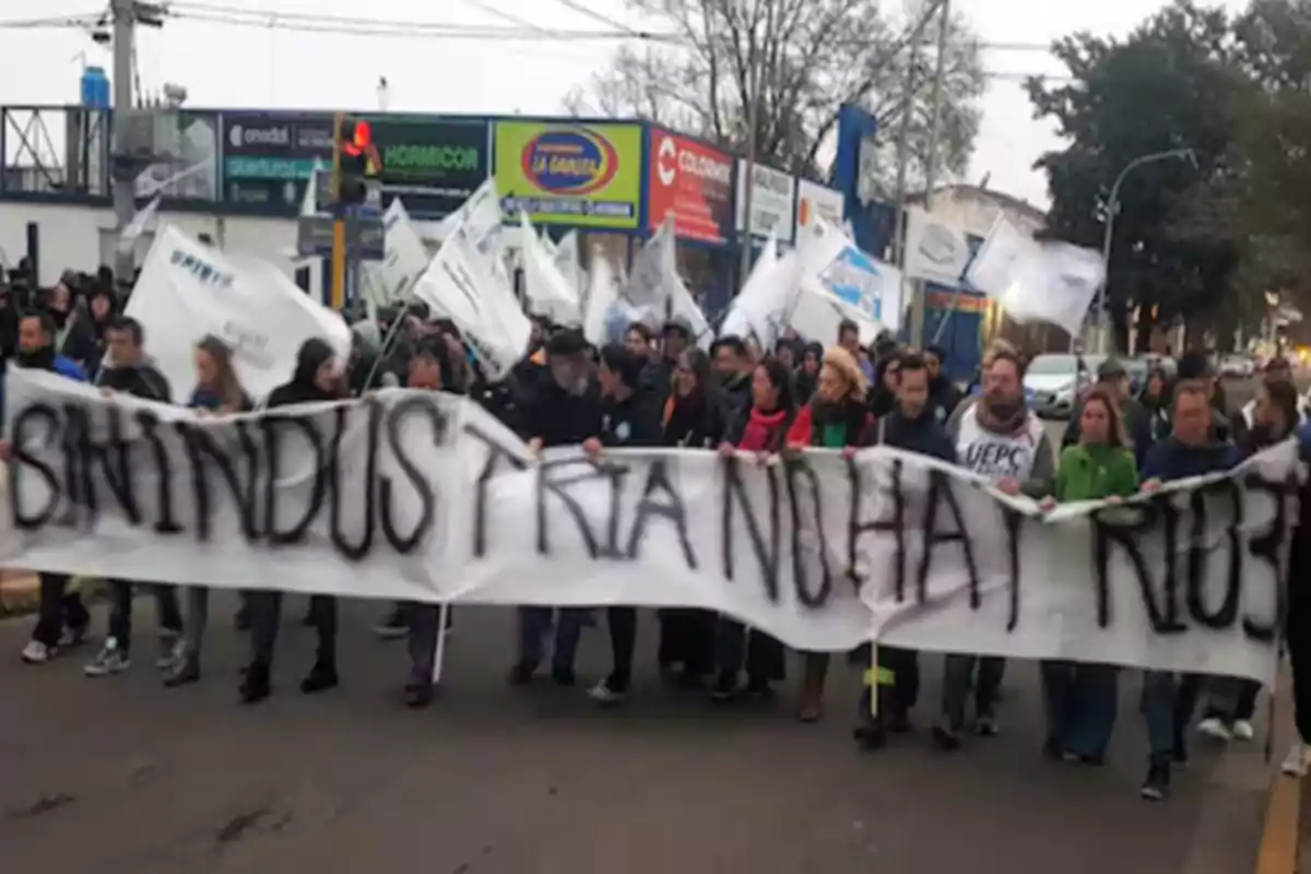Personas marchando por la calle con banderas y una pancarta que dice sin industria no hay ricos Personas marchando por la calle con banderas y una pancarta que dice sin industria no hay ricos