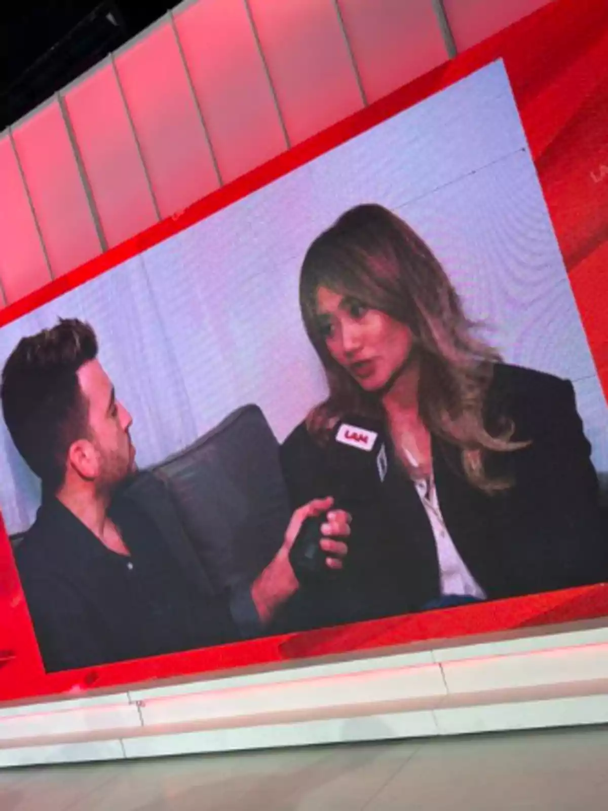 Pantalla gigante en un estudio de televisión mostrando una entrevista entre un hombre y una mujer Pantalla gigante en un estudio de televisión mostrando una entrevista entre un hombre y una mujer