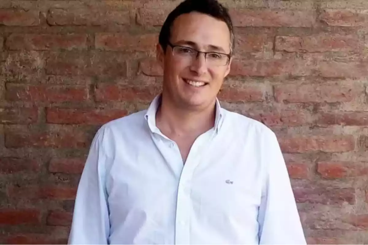 Hombre con gafas y camisa blanca sonriendo frente a una pared de ladrillos Hombre con gafas y camisa blanca sonriendo frente a una pared de ladrillos