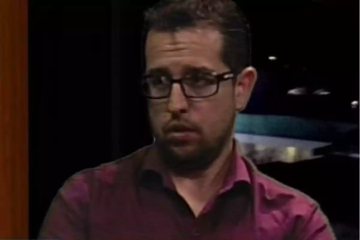 Hombre con barba y gafas usando una camisa burdeos mirando hacia un lado con expresión seria Hombre con barba y gafas usando una camisa burdeos mirando hacia un lado con expresión seria