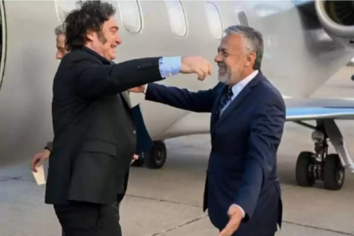 Dos hombres vestidos de traje se saludan sonrientes frente a un avión privado en una pista de aterrizaje