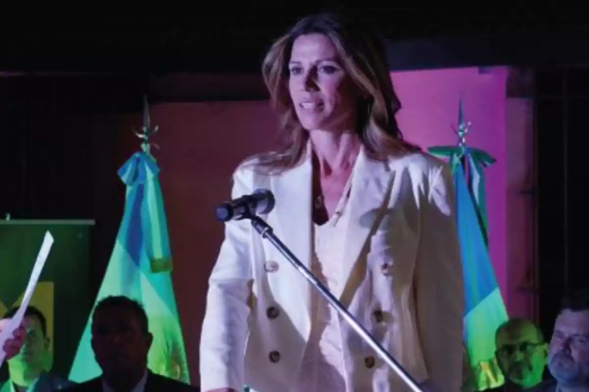 Long-haired blonde woman speaking into a microphone with Argentine flags in the background at a formal event Long-haired blonde woman speaking into a microphone with Argentine flags in the background at a formal event