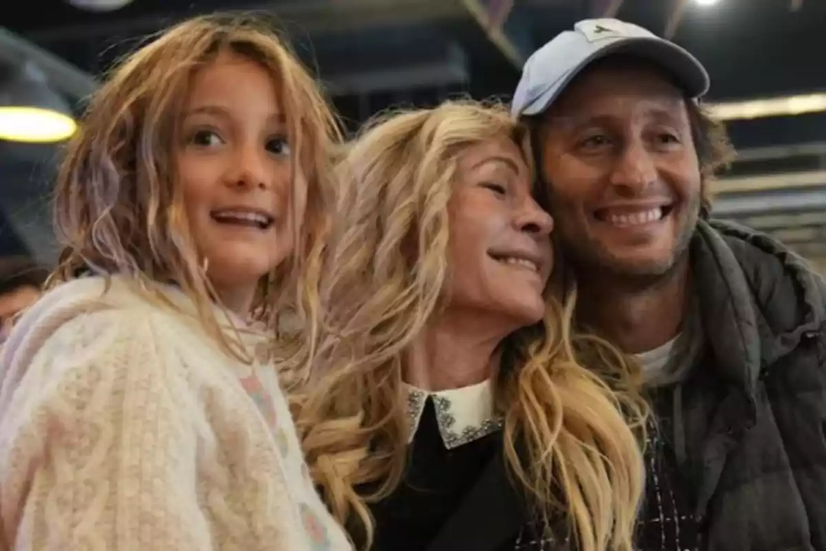 Three people smile and pose hugging each other in a well-lit indoor setting. Three people smile and pose hugging each other in a well-lit indoor setting.