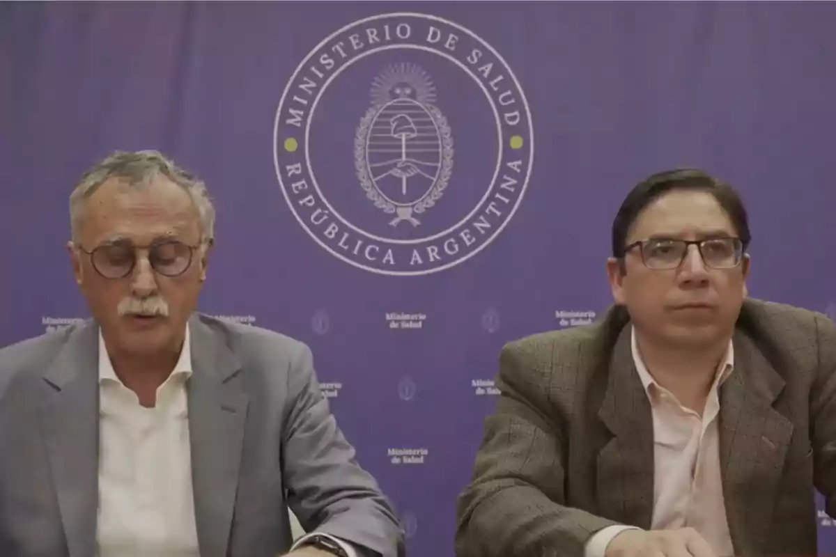Dos hombres sentados frente a un fondo violeta con el logo del Ministerio de Salud de la República Argentina