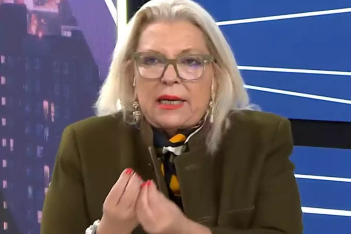 Blonde-haired woman with glasses speaking on a television show with a blue background and gesturing with her hands Blonde-haired woman with glasses speaking on a television show with a blue background and gesturing with her hands