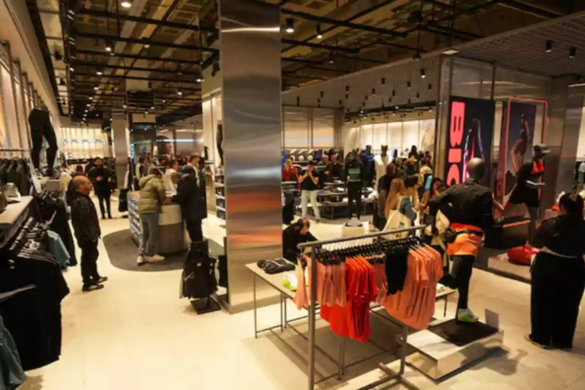 Tienda de ropa deportiva con varias personas comprando y maniquíes exhibiendo prendas Tienda de ropa deportiva con varias personas comprando y maniquíes exhibiendo prendas
