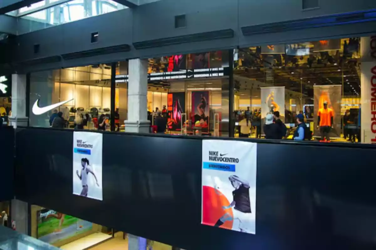 Fachada de una tienda Nike en un centro comercial con personas en el interior y carteles promocionales en el exterior