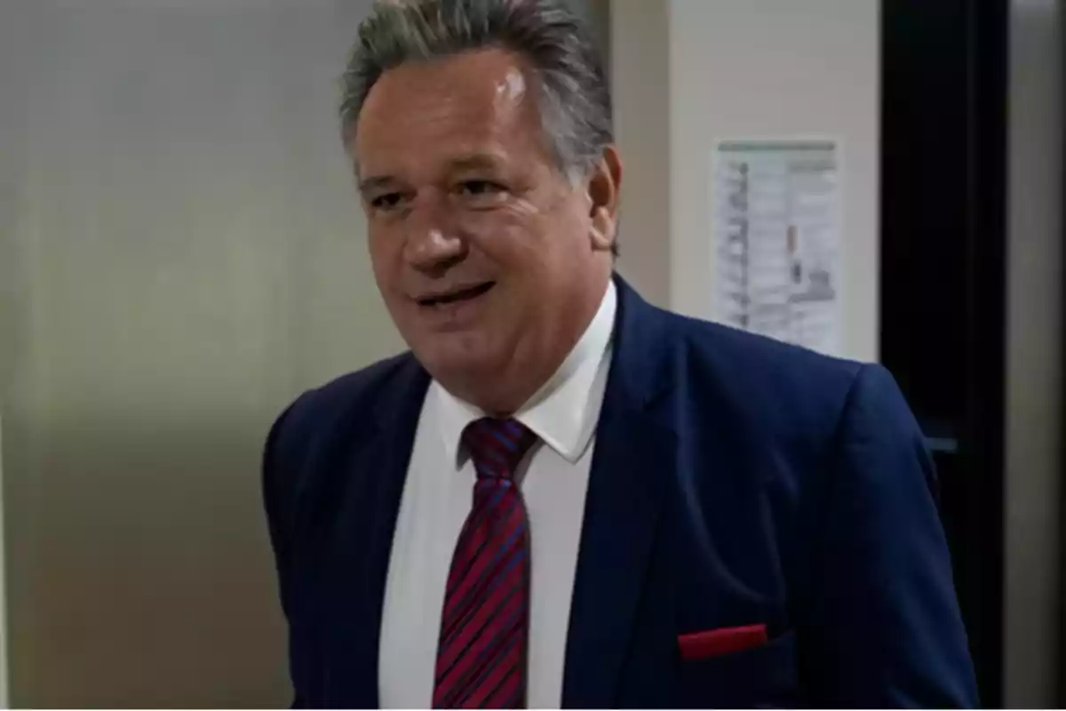 Middle-aged man with gray hair wearing a blue suit and red tie smiles in an office setting