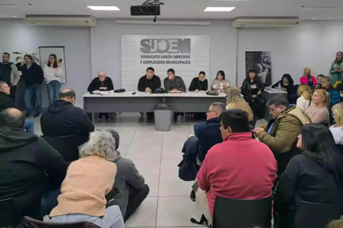 Reunión de un sindicato de empleados municipales con varias personas sentadas en círculo y una mesa principal al frente donde se encuentran los representantes del sindicato