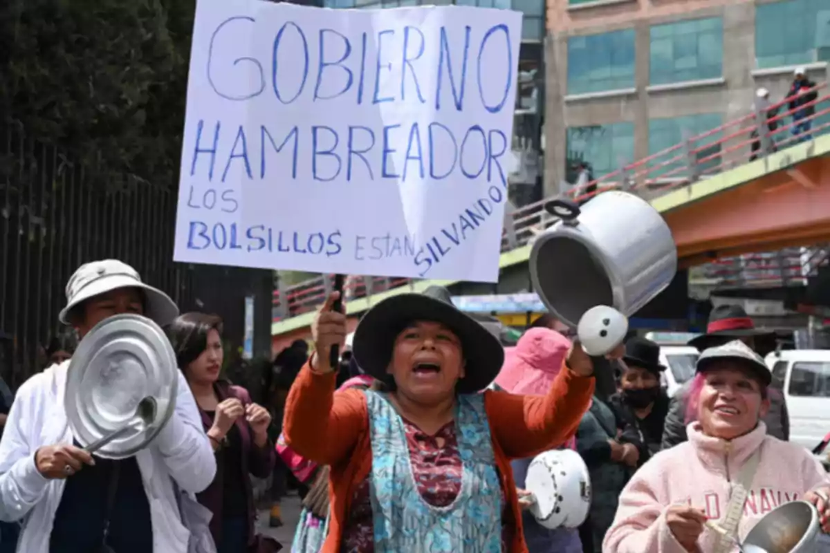 Mujeres protestan en la calle golpeando ollas y sartenes mientras una de ellas sostiene un cartel que critica al gobierno por la situación económica.